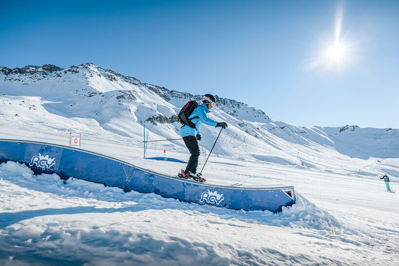 Skieur sur un rail du snowpark face aux sommets